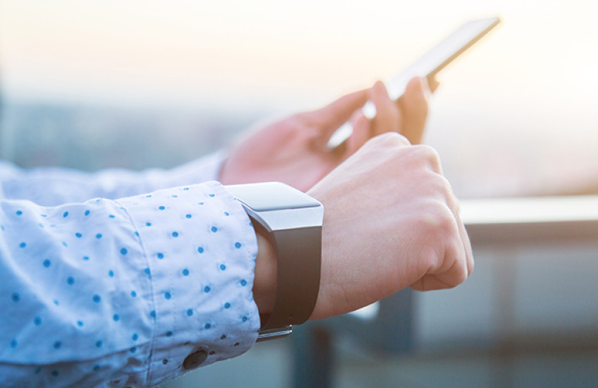 A person's hands, wearing a smart watch and holding a smart phone.