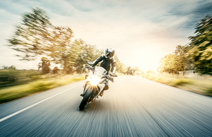 Motion blurred photo of a backlit motorcycle on a tree-lined road.