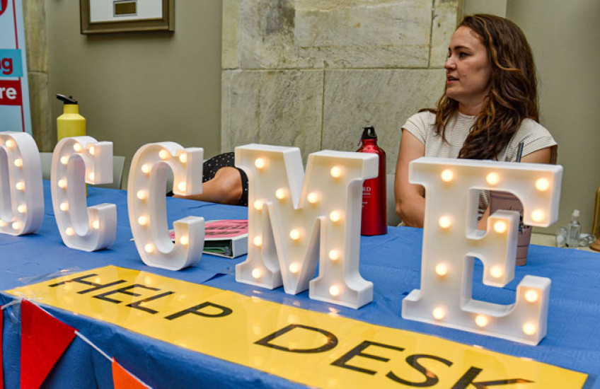 A women sits behind a table with lit up signage letters the spell out OCCME