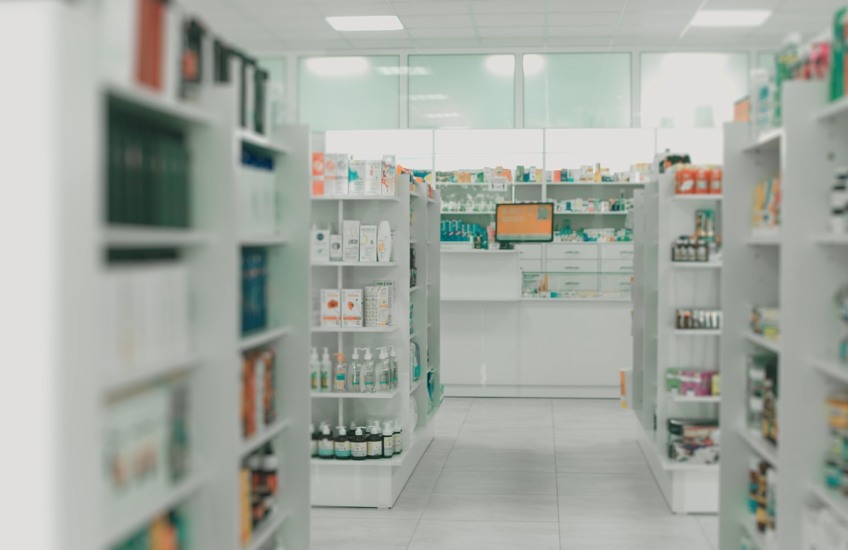 Shelves filled with medications in the aisles of a pharmacy draw the eye to the pharmacist’s prescription counter.
