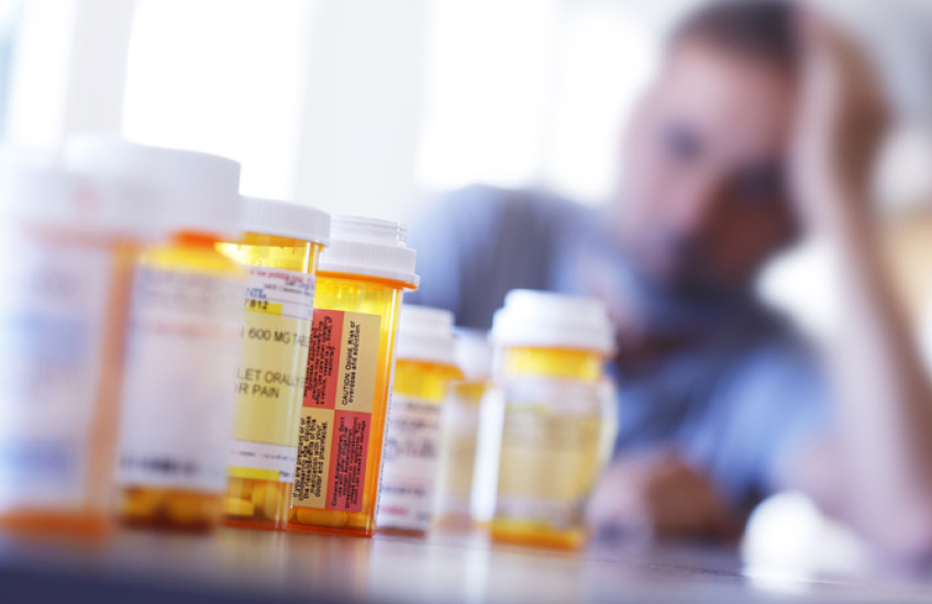 A blurry man in the background behind a row of prescription drugs.