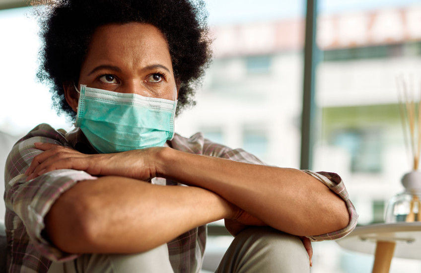 A woman wearing a surgical masks sits with her arms crossed
