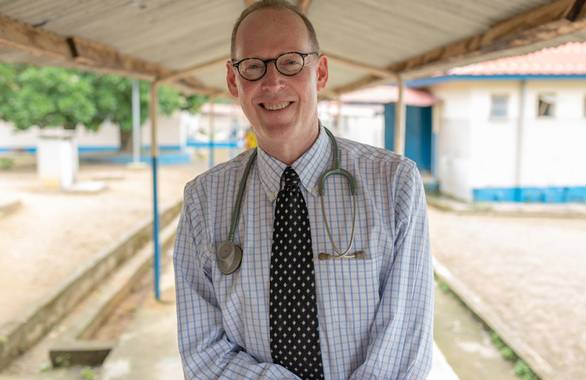 A man sits under a roof with a stethoscope draped around his shoulders.