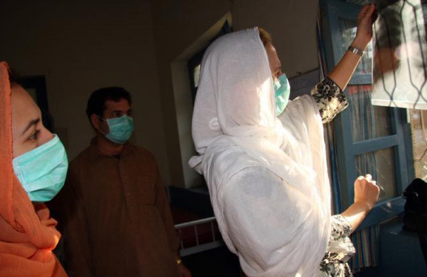Three people in surgical masks examine an x-ray of a person's lungs.