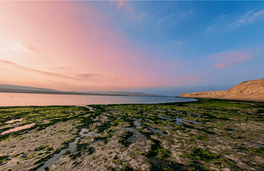 The sun setting over the ocean with a beach in the foreground.