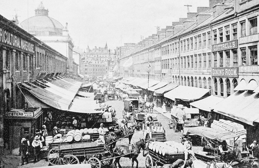 An antique black and white photo of the carts and stalls at Boston's Quincy Market from the 19th century. 