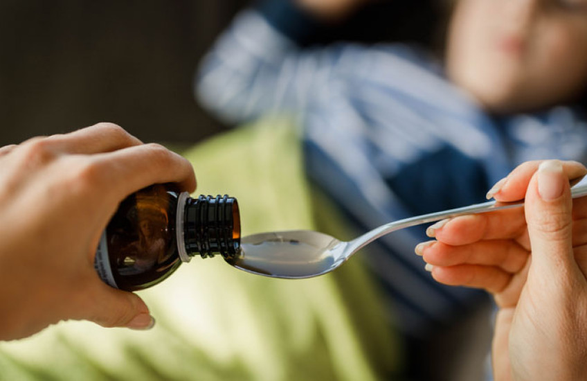 Closeup of adult women's hands pouring cough medicine into a spoon with child blurred out in background