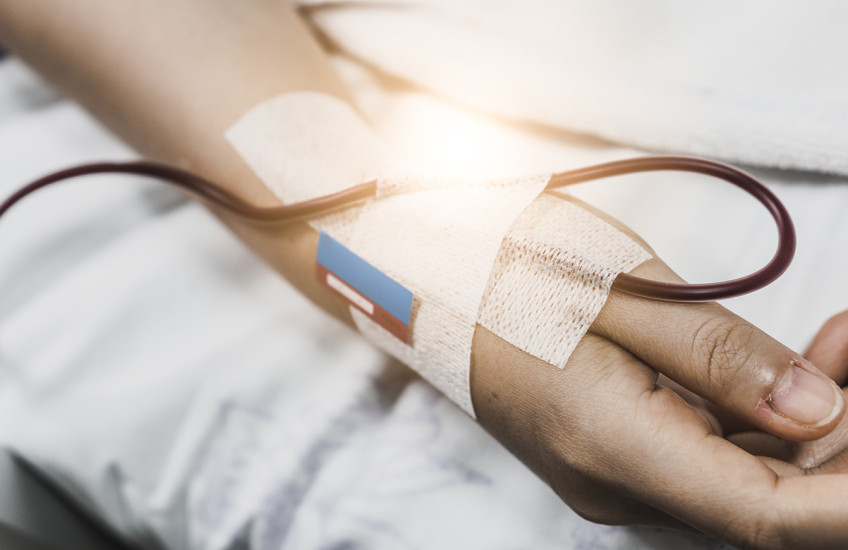 Close-up of a hospital patient's hand with a bandage and an IV tube. 
