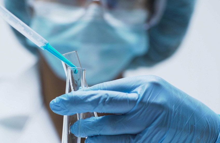 Person with mask and gloves pouring liquid into a test tube