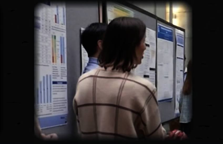 screen grab of video showing a person in front of a poster