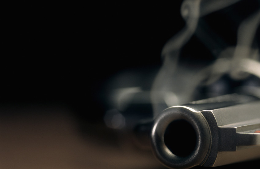 Narrow focus on the barrel of a smoking gun lying on the floor.