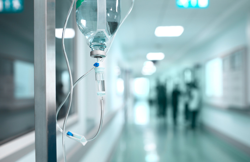 A bag of IV medicine hangs in a lonely hallway.