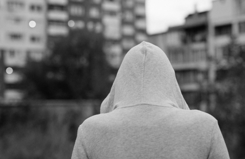 Black & white photo of person in a hooded sweatshirt, back facing camera in an urban setting