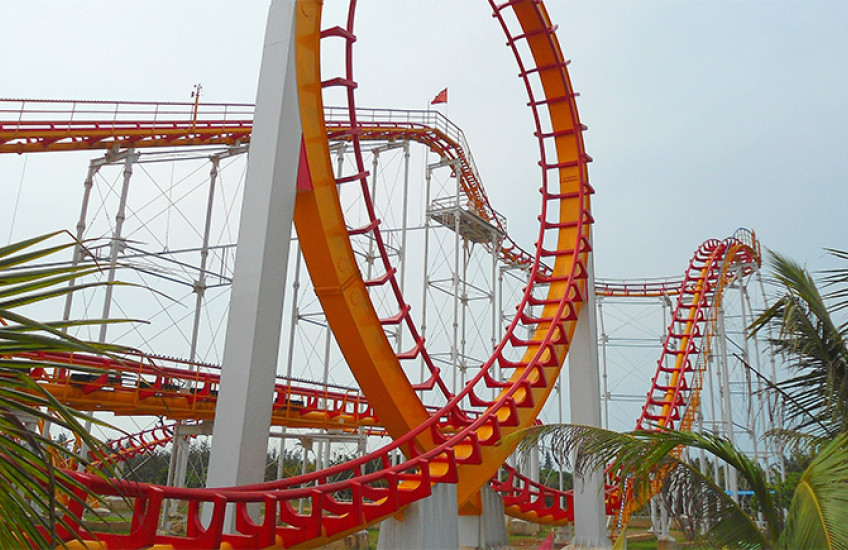 a roller coaster loops around in foreground, then rises and falls in the distance