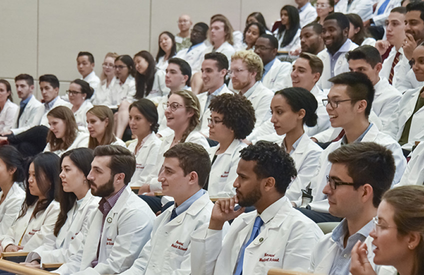 large group photo in auditorium of new students in white coats