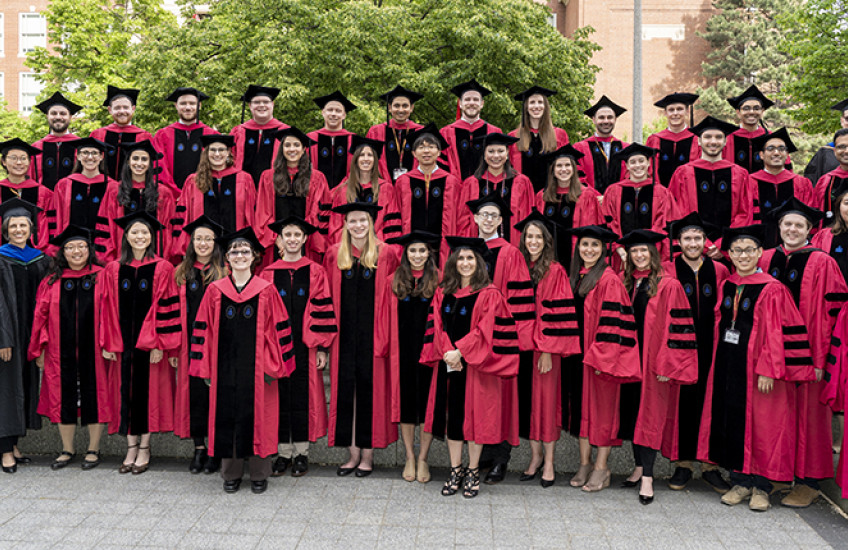dozens of doctoral recipients stand outside with program head and graduate dean
