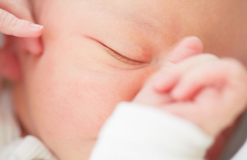 Closeup of a baby's face with one eye closed and hand resting on nose