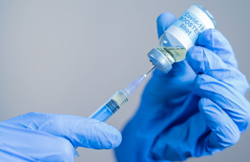 Hands in protective gloves putting a needle into a COVID-19 booster vaccine vial