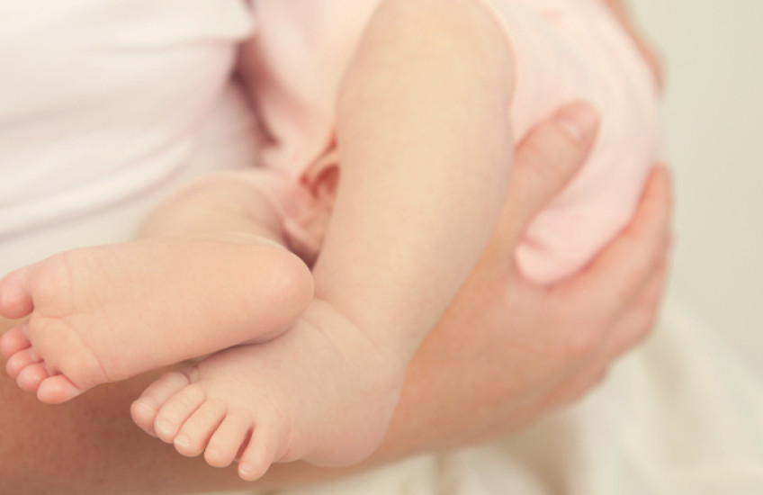 Photo of someone holding an infant, only the baby's feet and legs shown