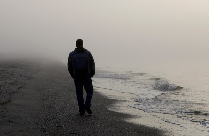 photo with silhouette of person walking on a foggy beach