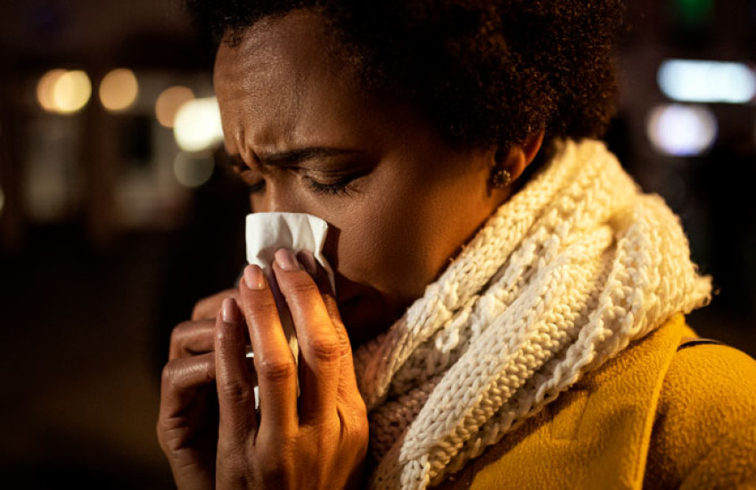 Closeup of woman in hat and scarf blowing nose into a tissue