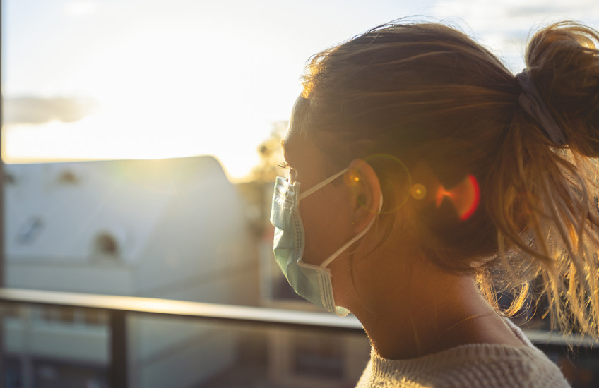 A woman  wearing a mask is seen in profile, backlit by the sun.