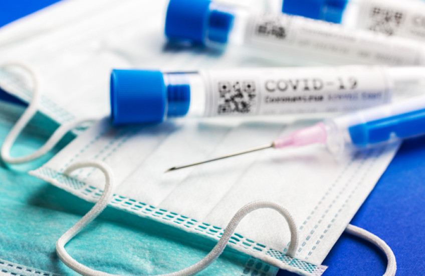 photo of medical mask, vials marked covid-19 and needle