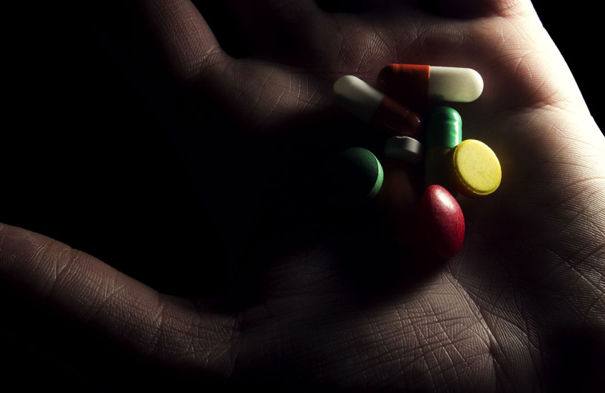 A shadowy hand holds a variety of pills.