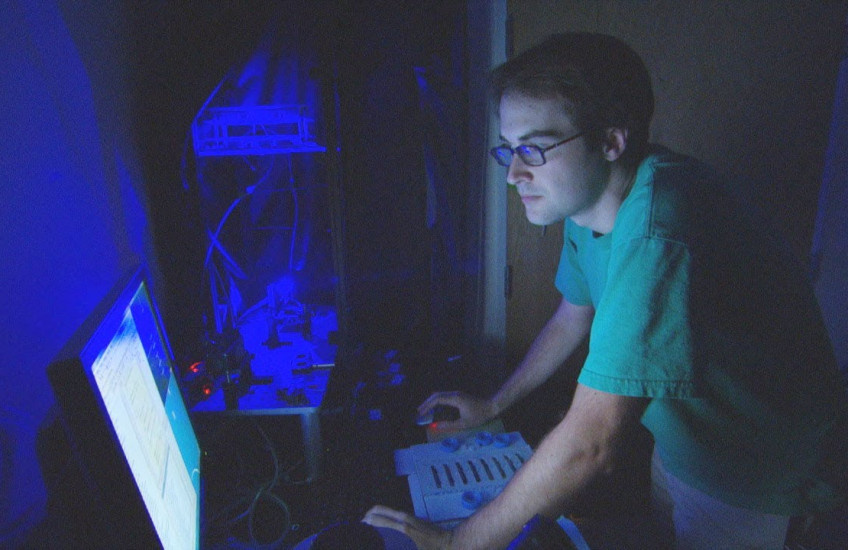 A man stands at a computer in the dark