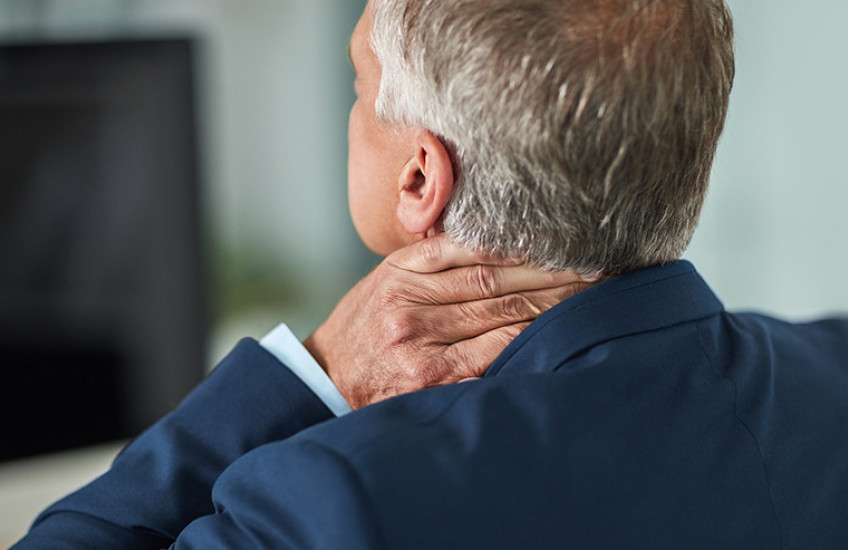 Back view of white man with gray hair in suit with tension holding neck