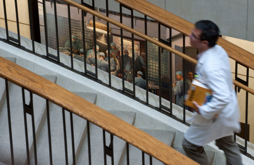 A student in a white coat runs up stairs