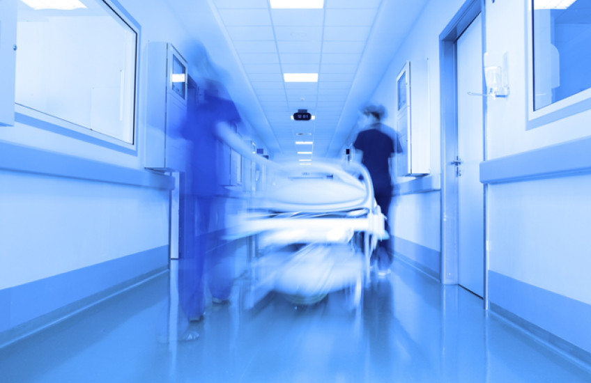 Hospital hallway with blurred figures & gurney.