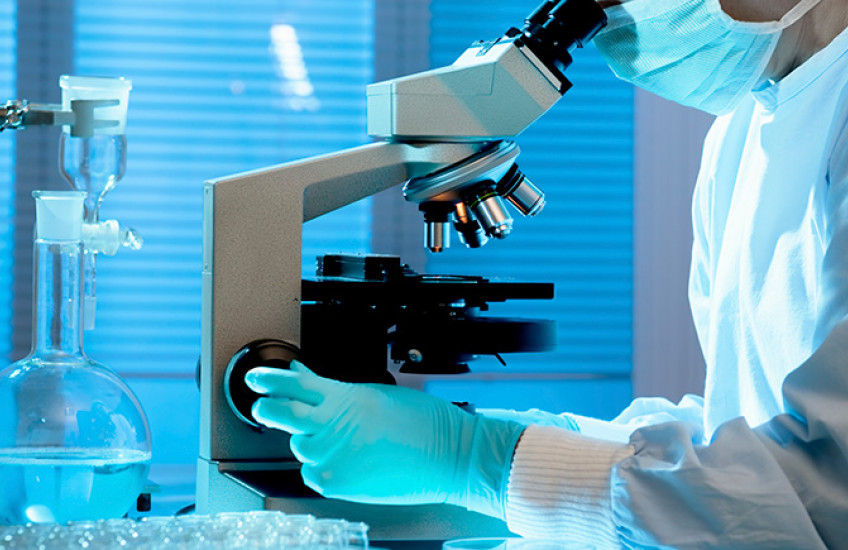 person at microscope in full PPE, face cropped out