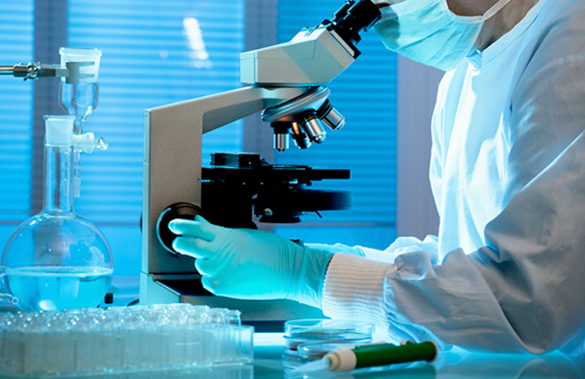 Stock image of a scientist wearing gloves handling a microscope.