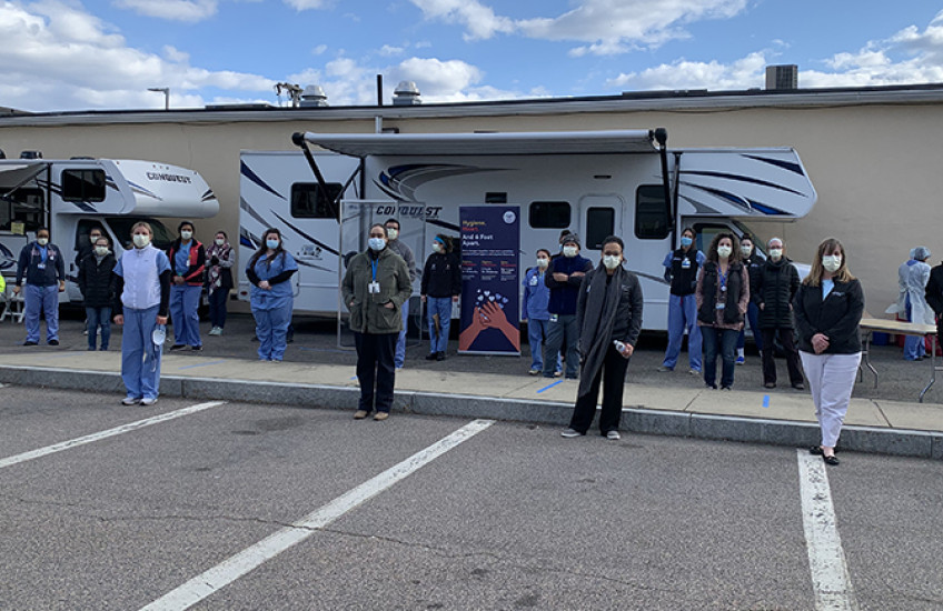 people wearing masks stand 6 feet apart in a parking lot with two RVs in background