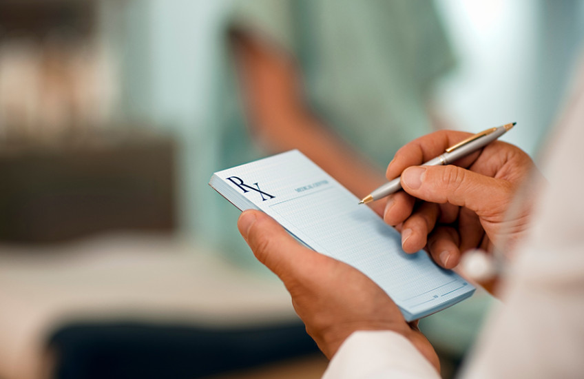 Doctor using a pen to fill out a prescription pad.
