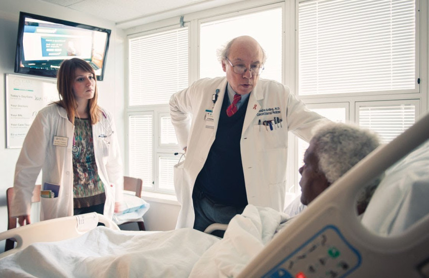Two doctors talk to a patient in a hospital room