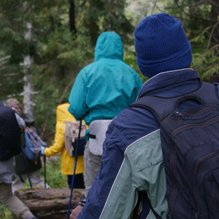 A group of young people hiking in the woods wearing jackets and hats.