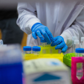 : Scientist wearing a white coat and blue gloves working in a lab setting.