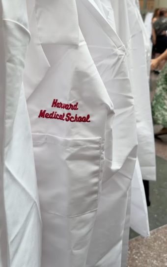 Close-up view of crisp white coats on a hanger with "Harvard Medical School" embroidered on the placket