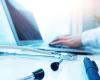 Close-up of a laptop, stethoscope, and physician’s forearm in white coat