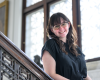 A woman leans on a banister and smiles at the camera