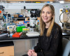 A researcher sits on a chair next to a microscope in a lab space