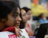 Focus on one student leaning on laptop with an HST sticker on the cover with several students in blurred background.