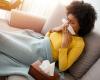 A sick person blowing their nose on a couch