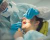 Dentist in full PPE with his hands inside a female patient's open mouth