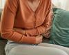 The torso of a sitting person hunched over with their arms wrapped across their stomach