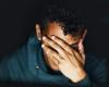 A close up of a person with their hand covering their face against a black background