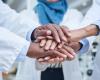 Close up of the stacked hands of three physicians with different ethnicities in solidarity.