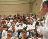 Sideview of Chang in white coat holding mic while speaking to audience of students, many in white coats